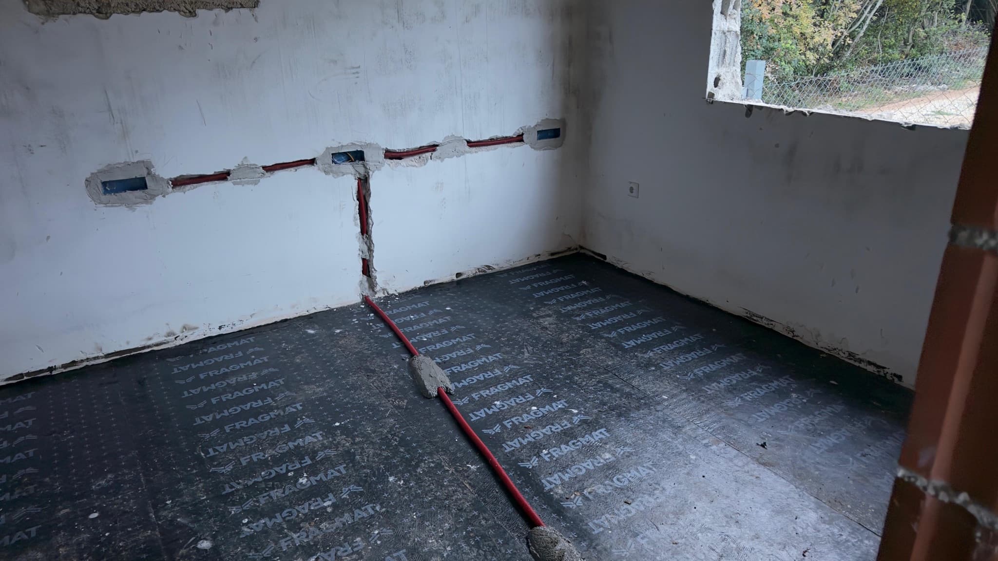 A conduit run laid over floor insulation next to prepared wall boxes.