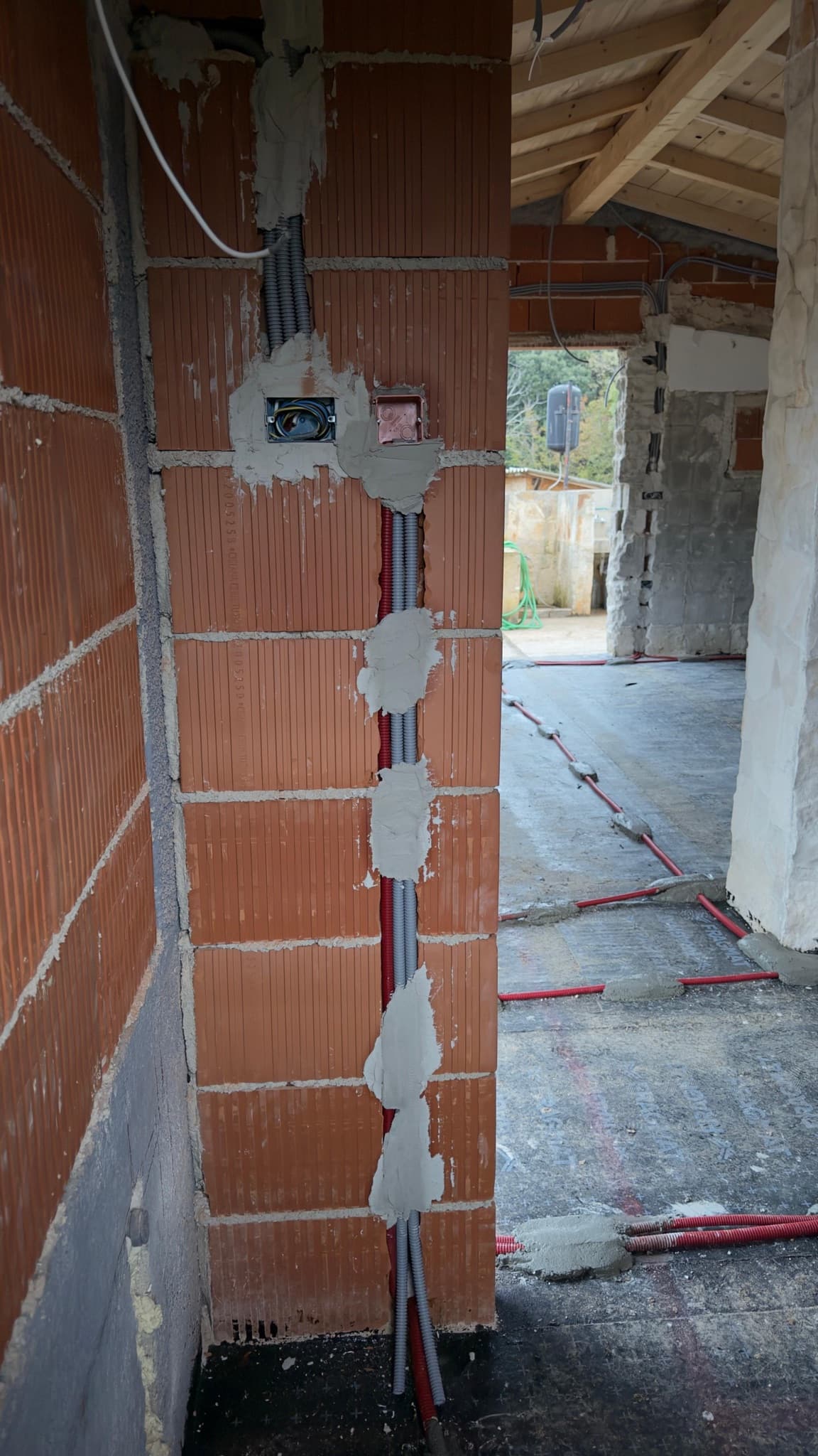 A vertical conduit run chased into a block wall and closed with plaster.