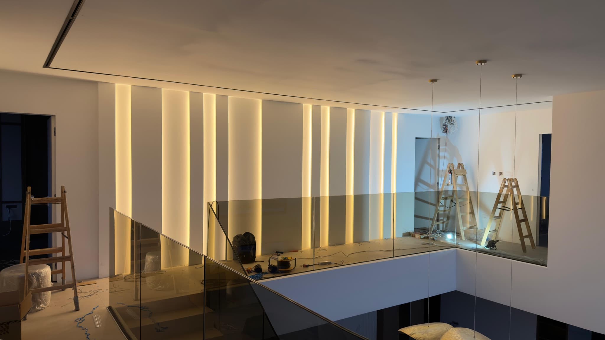 Vertical LED strips recessed into the wall beside a family home's gallery with a glass balustrade.