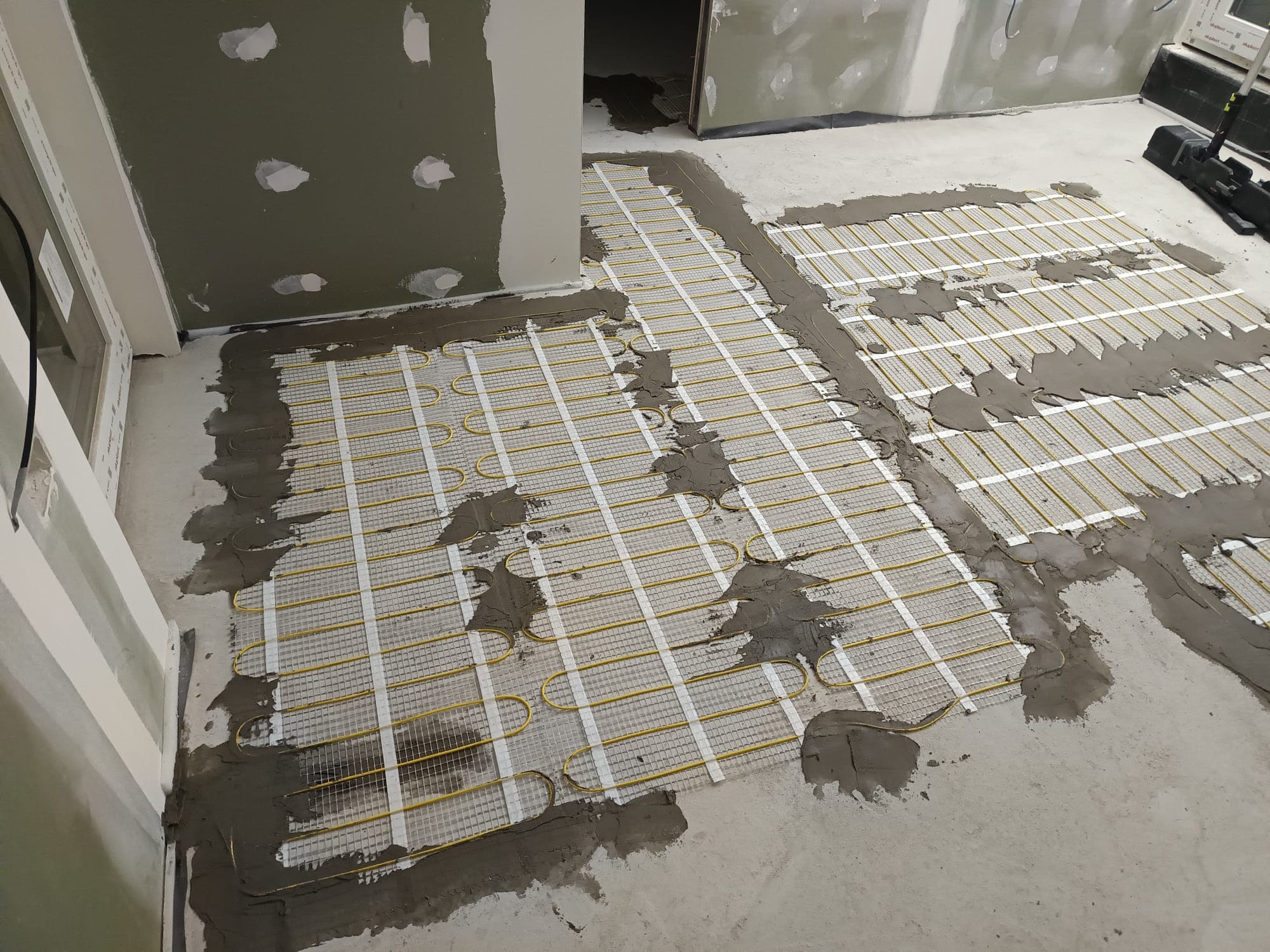 Several runs of heating mat bedded in adhesive during an underfloor heating installation.