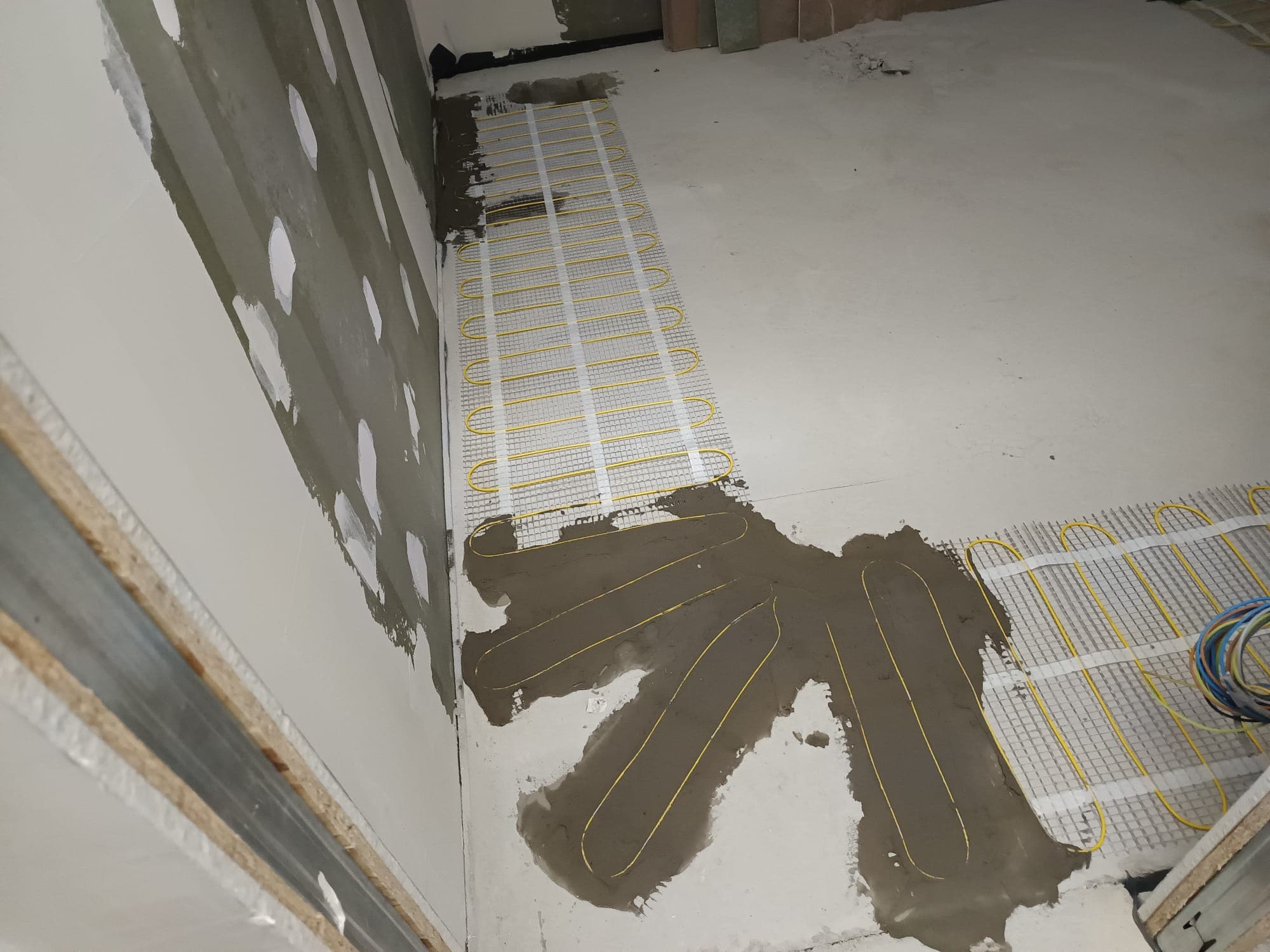 A strip of heating mat laid along a bedroom wall with the connecting cable run in place.