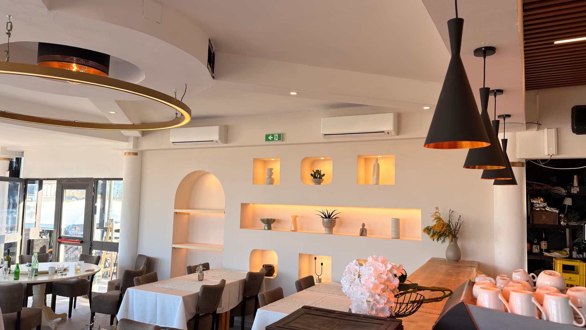 Restaurant interior with a ring chandelier and lit wall niches.