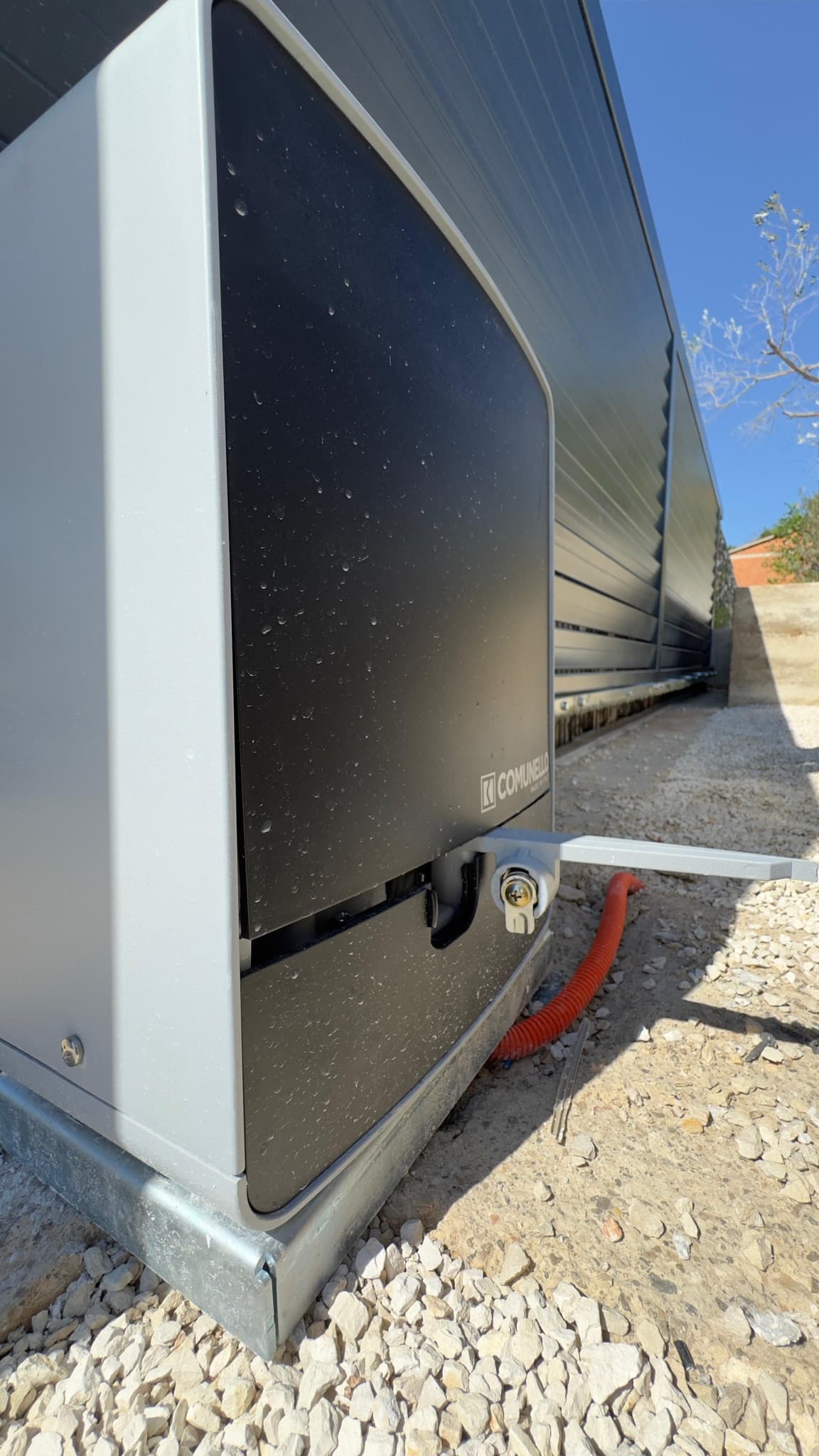 Sliding gate drive motor in its protective housing, mounted on a base beside the gate leaf.